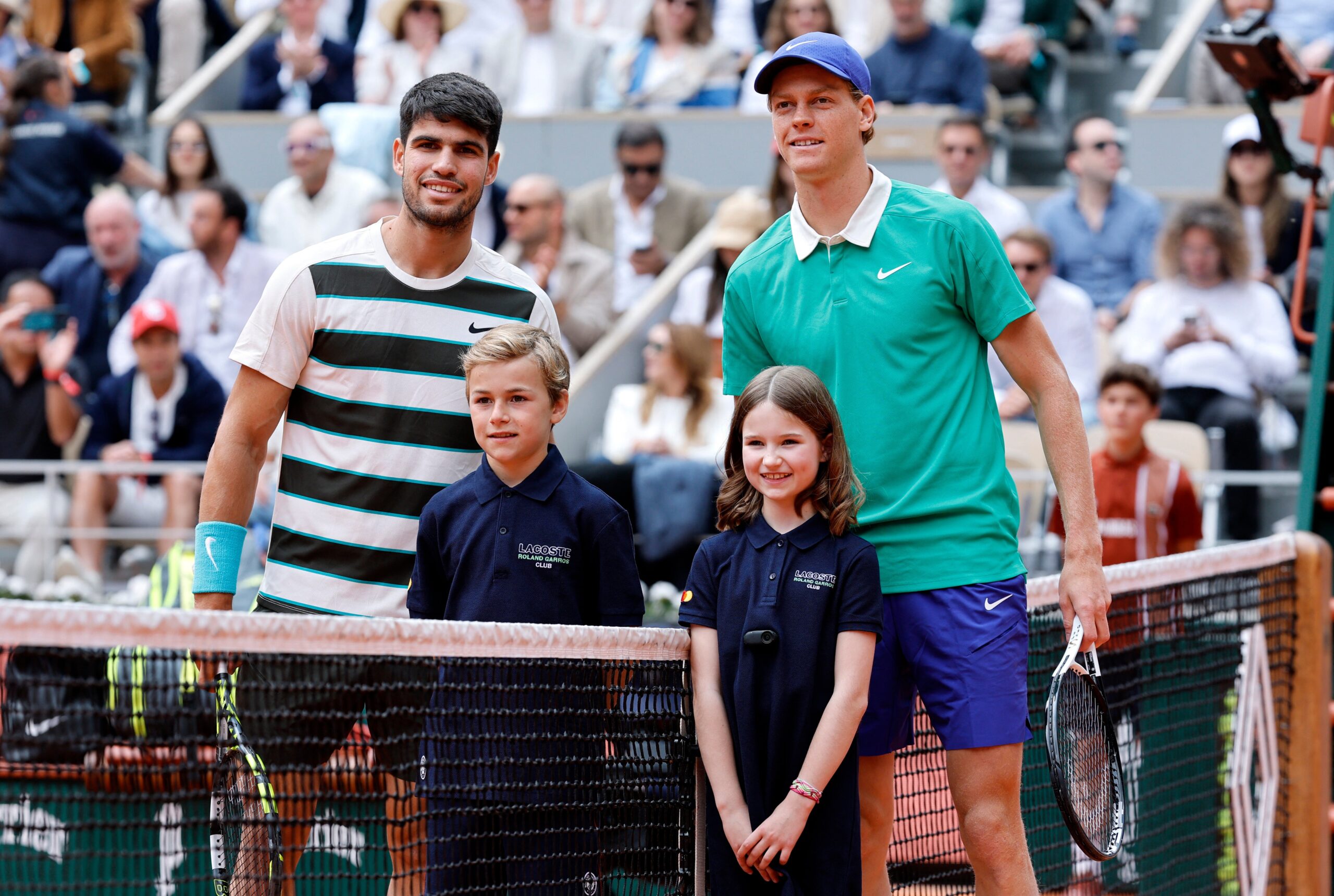 Carlos Alcaraz and Jannik Sinner pose with young fans before the French Open 2025 final match at Roland Garros.