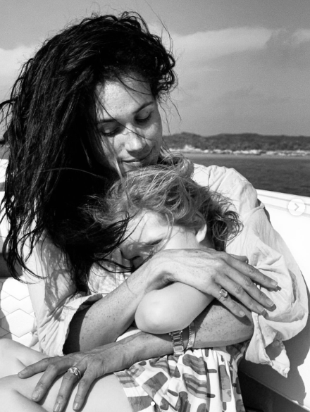 Meghan Markle smiling while holding their daughter, Princess Lilibet, during a trip.